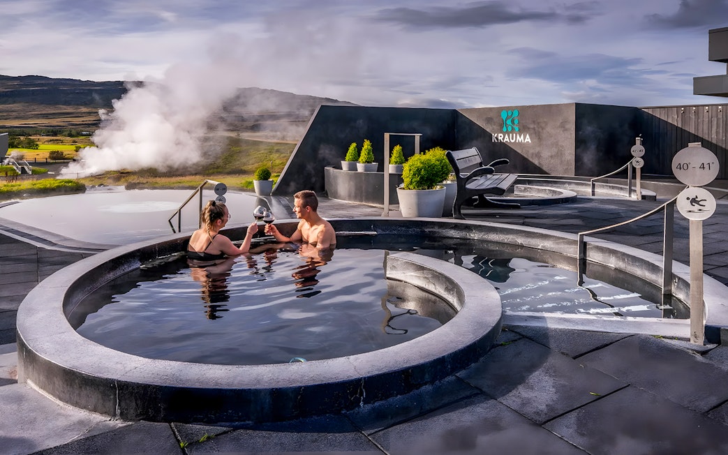Couple enjoying Krauma Geothermal Baths in Iceland with steam rising in the background.
