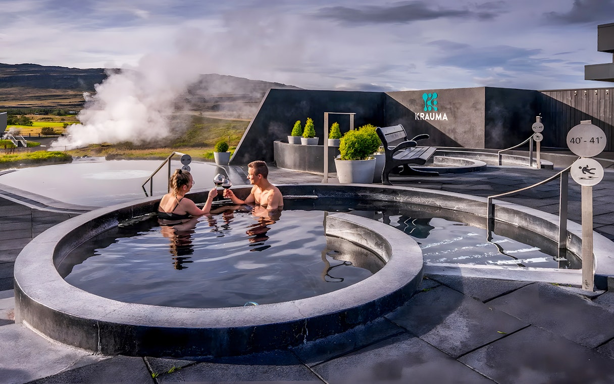 Couple enjoying Krauma Geothermal Baths in Iceland with steam rising in the background.