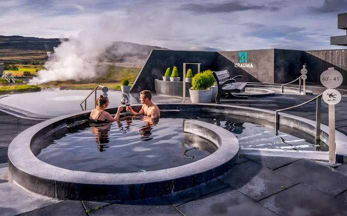 Couple enjoying Krauma Geothermal Baths in Iceland with steam rising in the background.