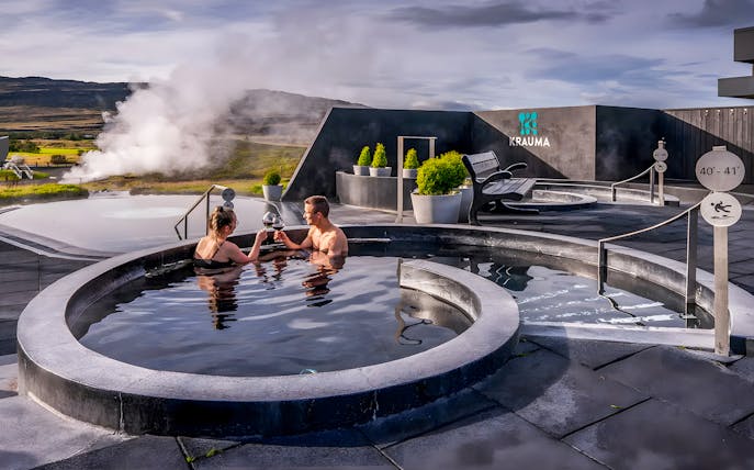 Couple enjoying Krauma Geothermal Baths in Iceland with steam rising in the background.