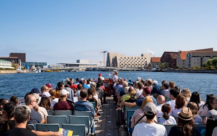 Tourists on a boat tour in Copenhagen, viewing waterfront architecture and landmarks.
