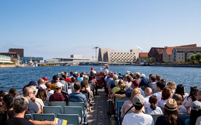 Tourists on a boat tour in Copenhagen, viewing waterfront architecture and landmarks.
