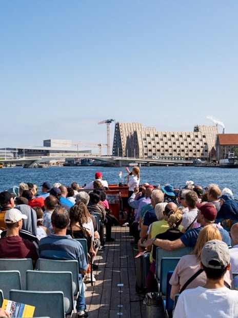 Tourists on a boat tour in Copenhagen, viewing waterfront architecture and landmarks.