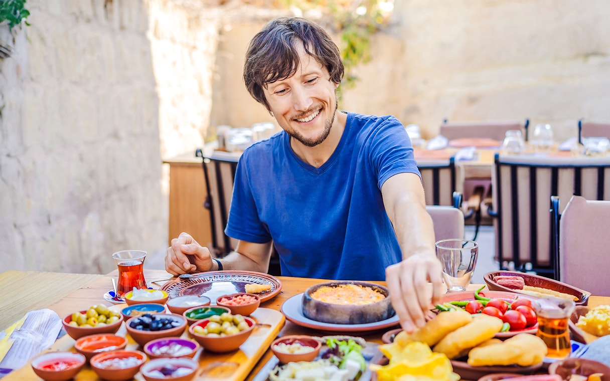 Man enjoying Turkish breakfast with various dishes and tea.