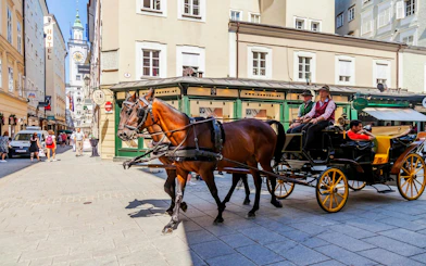 Horse-drawn carriage on a street in Salzburg, Austria, with historic buildings in the background.