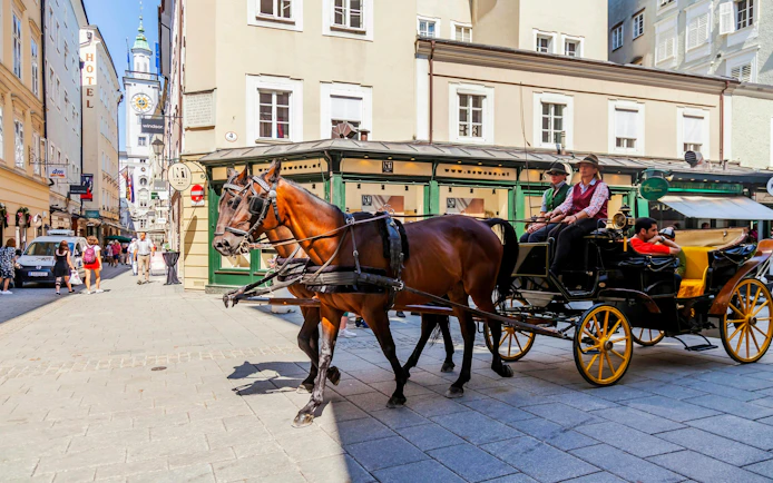 Horse-drawn carriage on a street in Salzburg, Austria, with historic buildings in the background.
