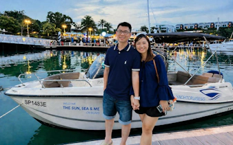 Couple standing by YachtCruiseSG speedboat at marina, Singapore evening lights reflecting on water.
