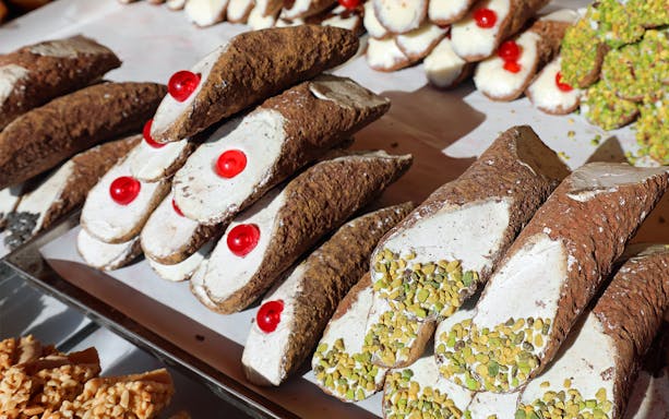 Cannoli with cherries and pistachios on display during a street food tour in Palermo.