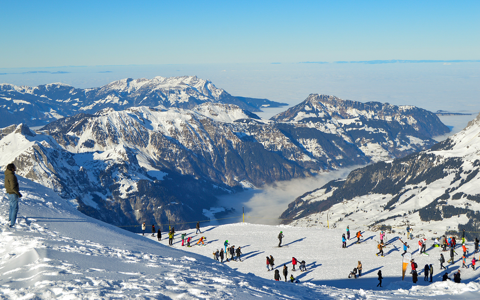 Skiers and tourists on snowy Mount Titlis with panoramic views of the Swiss Alps.