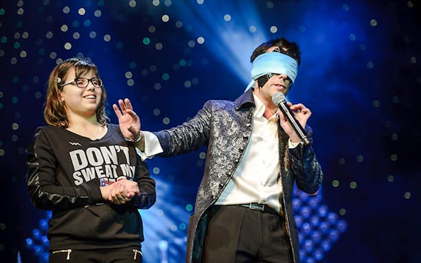 Performer with blindfold and audience member on stage at Frederick Da Silva Vegas show.