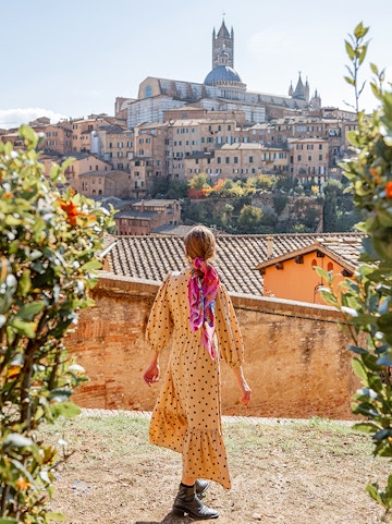 Woman walking towards Siena Cathedral in Tuscany, Italy, surrounded by historic buildings.