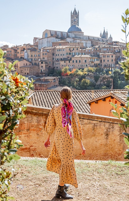 Woman walking towards Siena Cathedral in Tuscany, Italy, surrounded by historic buildings.