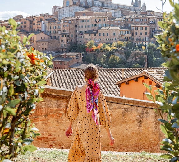 Woman walking towards Siena Cathedral in Tuscany, Italy, surrounded by historic buildings.