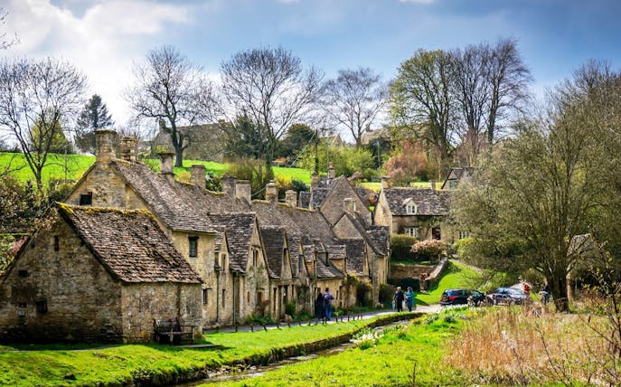 Cotswolds village scene with stone cottages and visitors walking along a path.