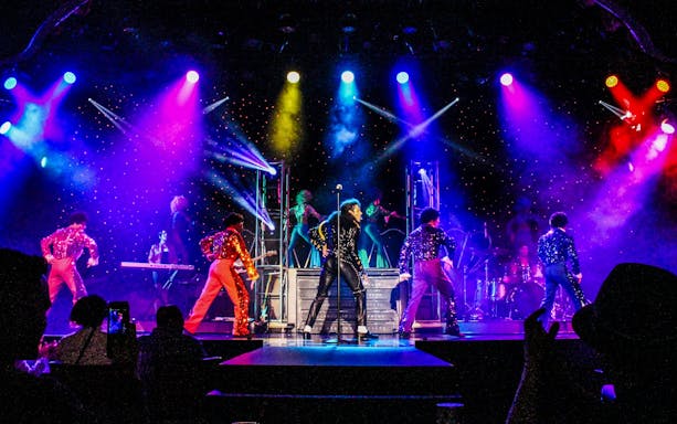 Stage performance of MJ Live in Vegas with dancers in colorful costumes.