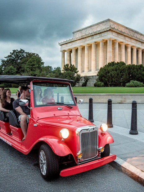 Guests touring Washington D.C. in a red electric roadster near the Lincoln Memorial at night.