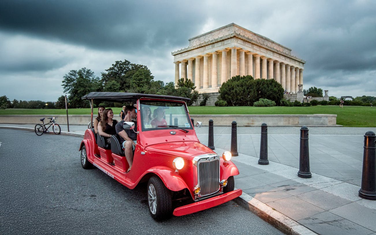 Guests touring Washington D.C. in a red electric roadster near the Lincoln Memorial at night.