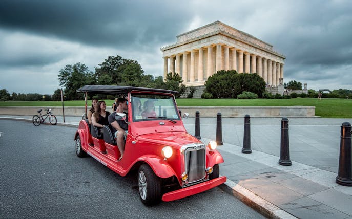 Guests touring Washington D.C. in a red electric roadster near the Lincoln Memorial at night.