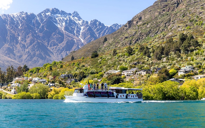 Cruise boat on Lake Wakatipu with passengers viewing Queenstown's Remarkables mountains.