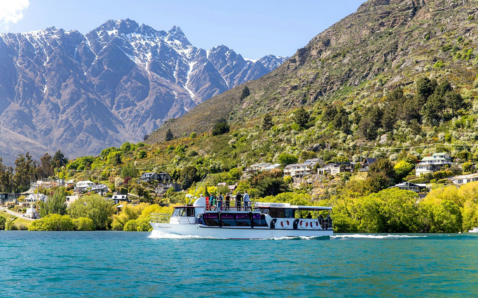 Cruise boat on Lake Wakatipu with passengers viewing Queenstown's Remarkables mountains.