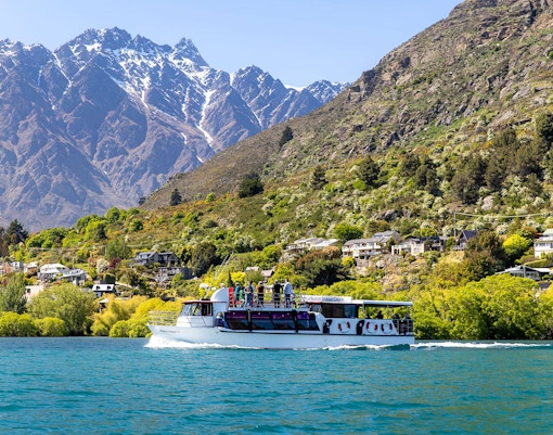 Cruise boat on Lake Wakatipu with passengers viewing Queenstown's Remarkables mountains.