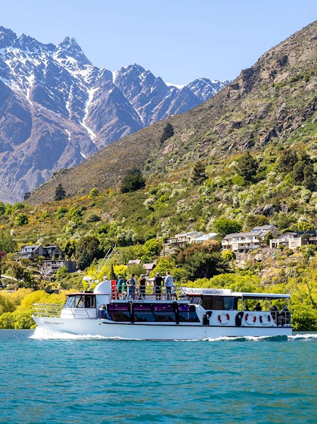 Cruise boat on Lake Wakatipu with passengers viewing Queenstown's Remarkables mountains.