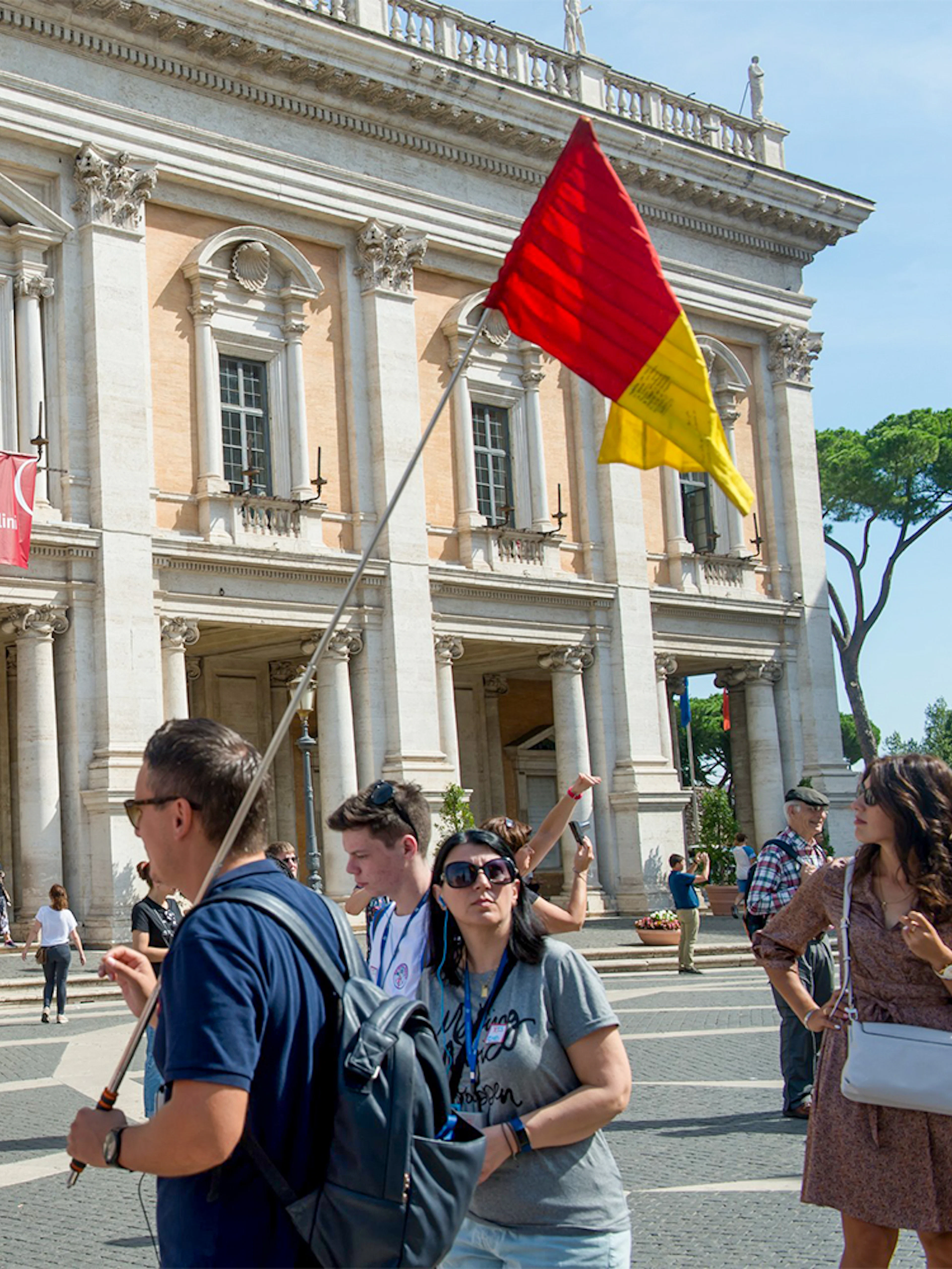 Tour group outside Capitoline Museums in Rome with guide holding flag.