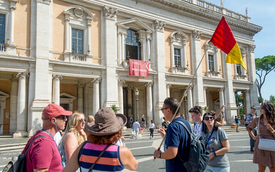 Tour group outside Capitoline Museums in Rome with guide holding flag.