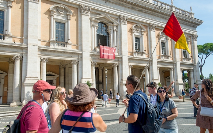 Tour group outside Capitoline Museums in Rome with guide holding flag.