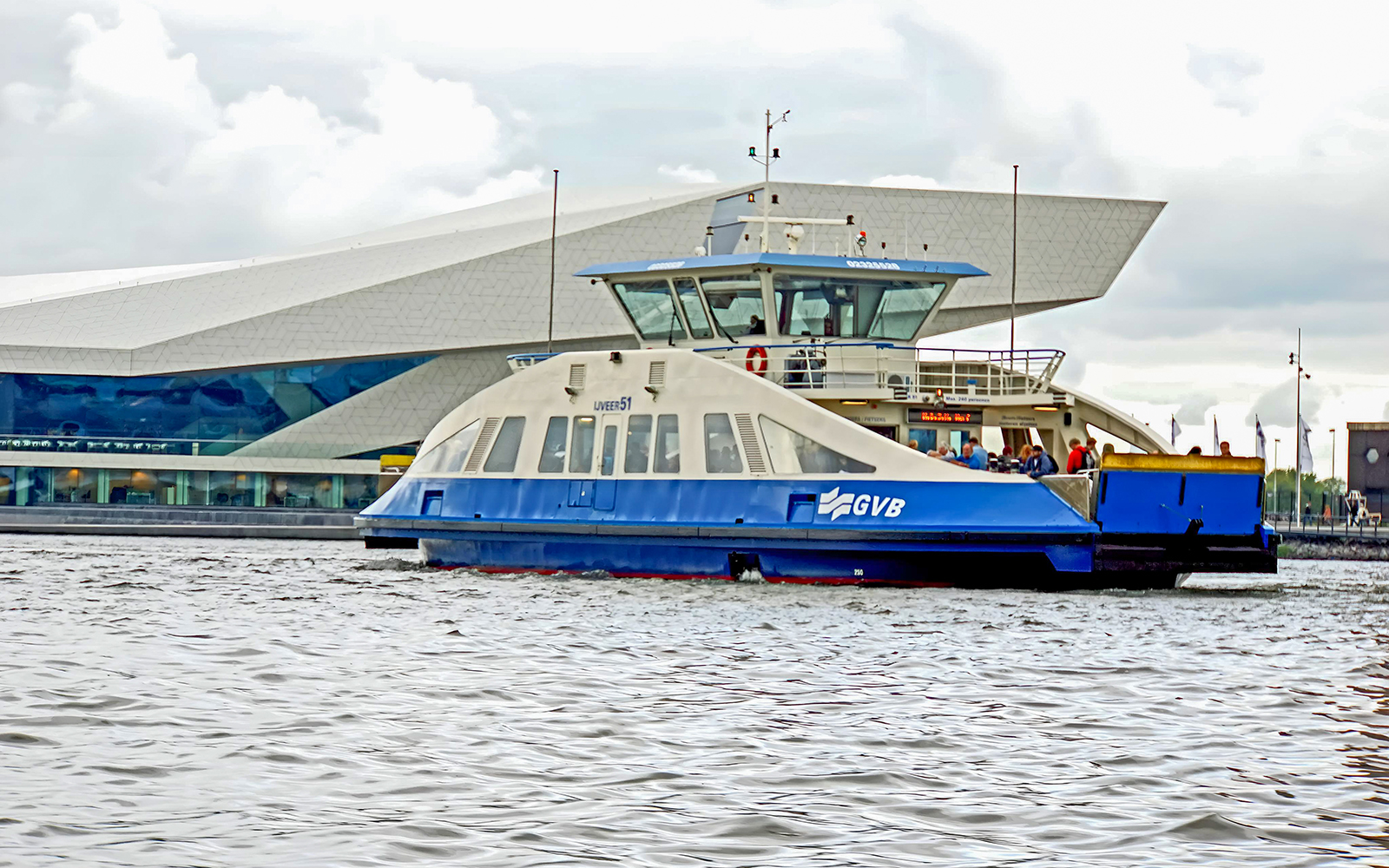 GVB ferry on Amsterdam canal near modern building.