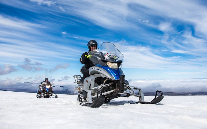 Snowmobile ride on Langjokull Glacier under clear blue sky.