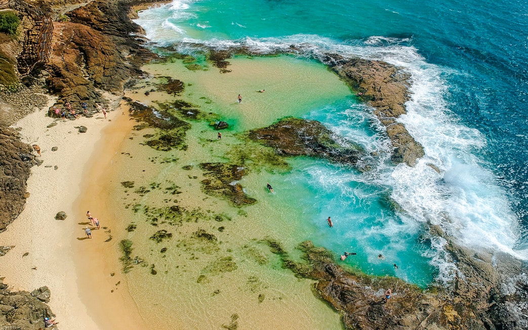 Aerial view of people snorkeling in turquoise waters at Fraser Island, K'gari, near rocky shoreline.