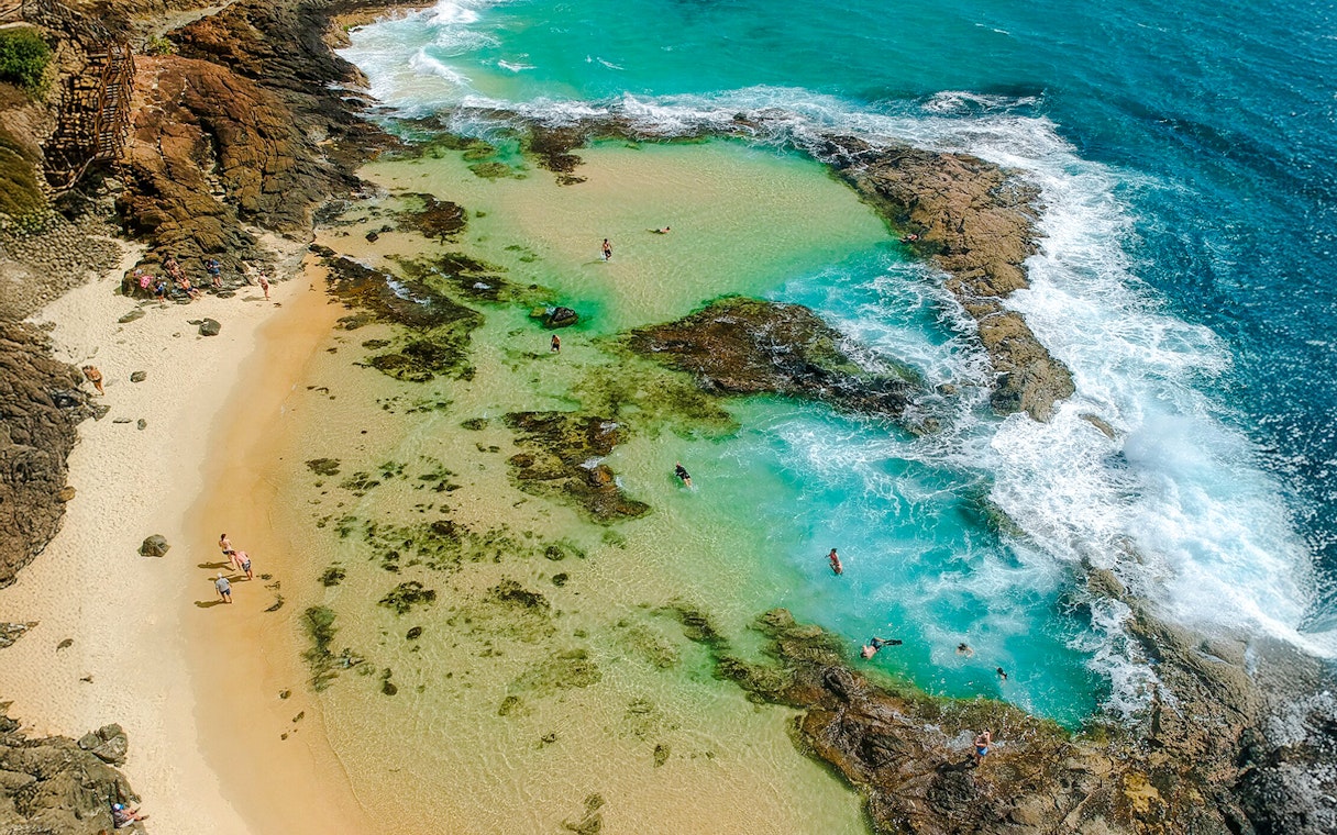 Aerial view of people snorkeling in turquoise waters at Fraser Island, K'gari, near rocky shoreline.