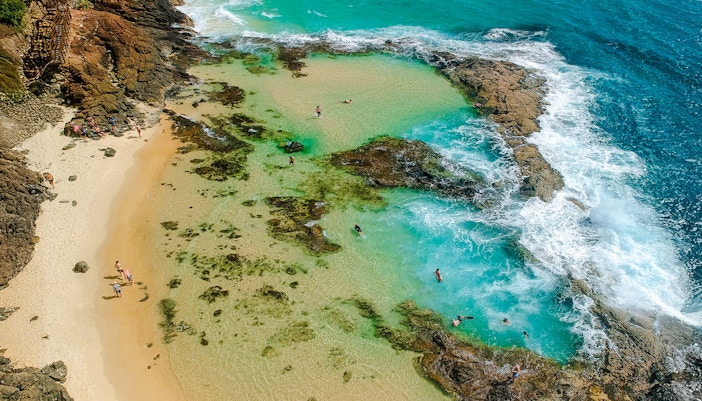 Aerial view of people snorkeling in turquoise waters at Fraser Island, K'gari, near rocky shoreline.