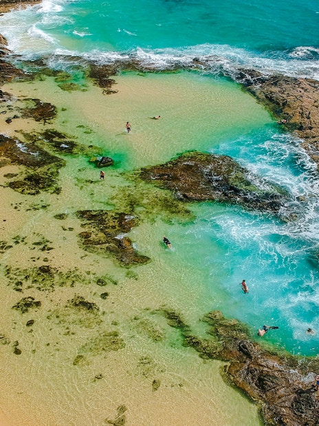 Aerial view of people snorkeling in turquoise waters at Fraser Island, K'gari, near rocky shoreline.