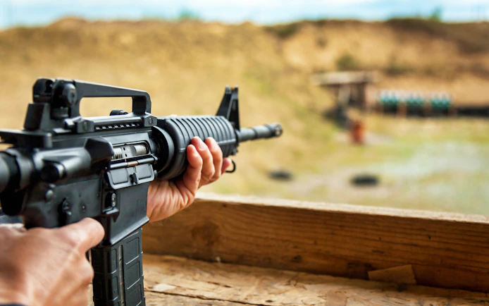 Person aiming rifle at outdoor shooting range.