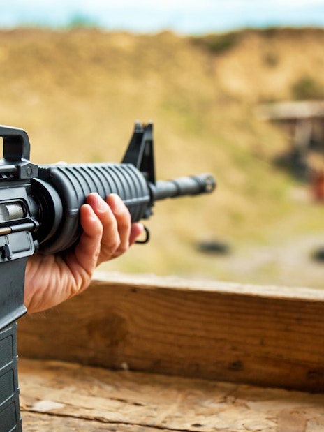 Person aiming rifle at outdoor shooting range.