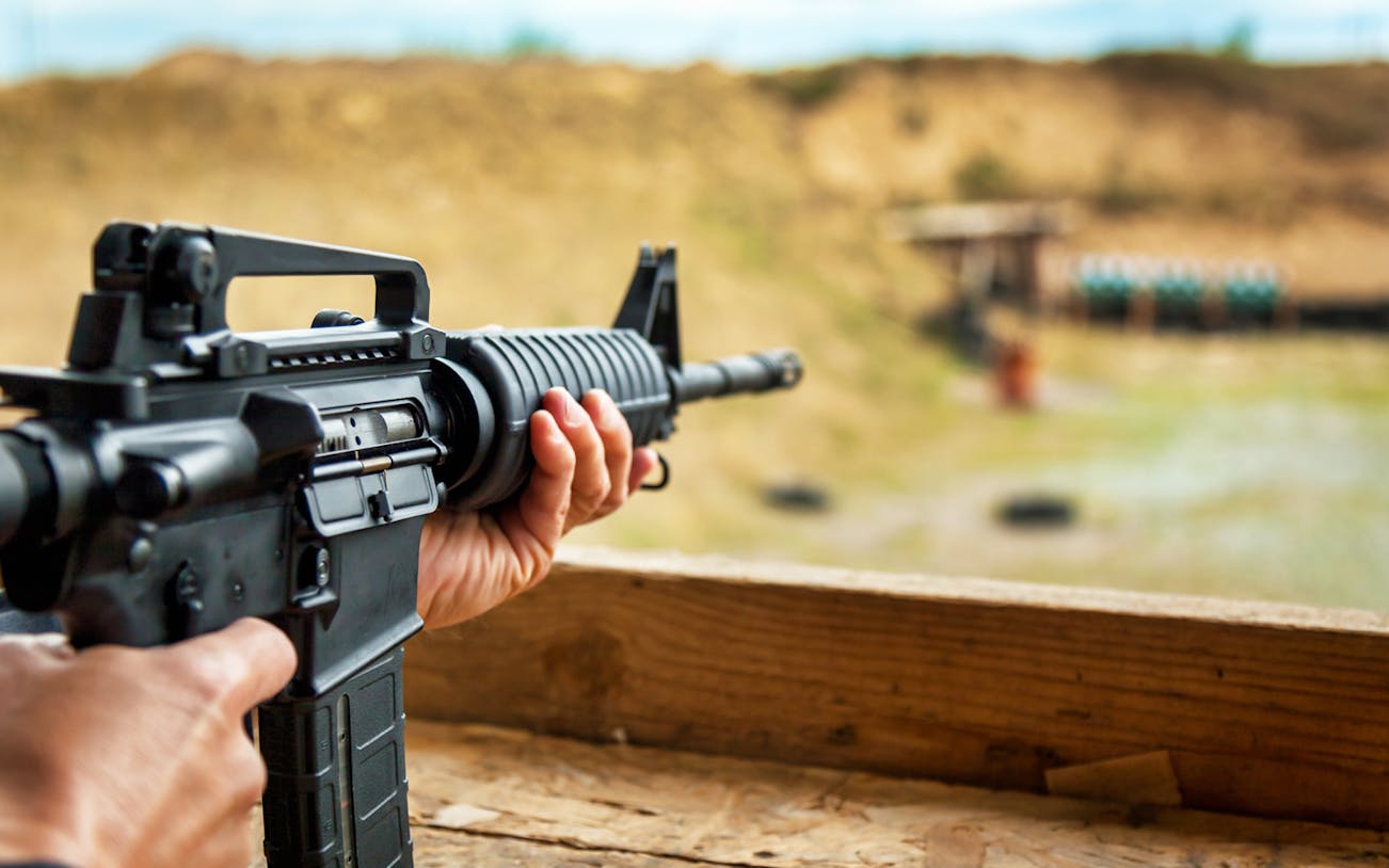 Person aiming rifle at outdoor shooting range.