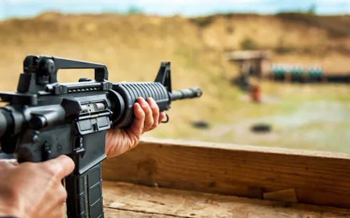 Person aiming rifle at outdoor shooting range.
