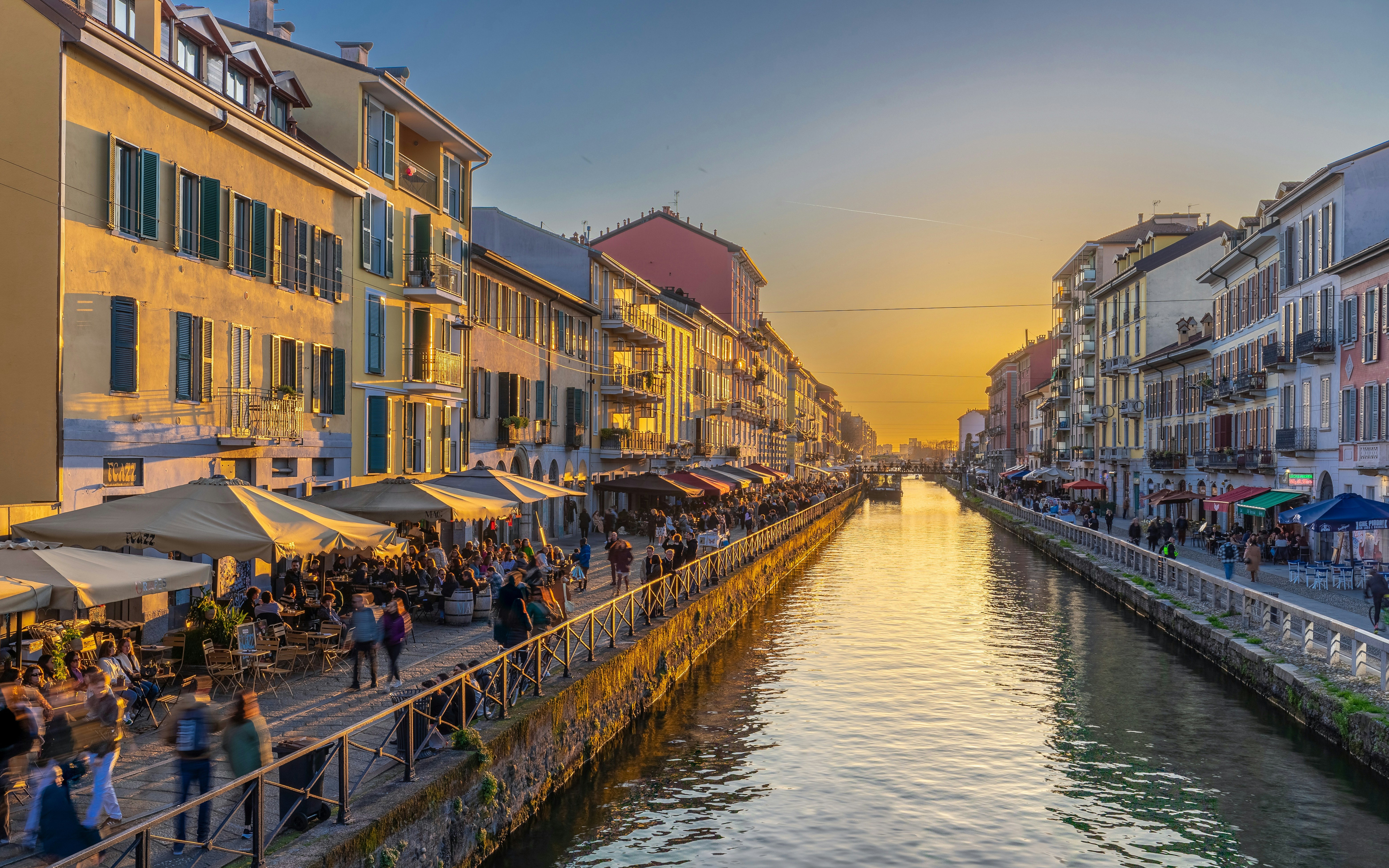 Navigli canals in Milan at sunset with bustling cafes and people strolling along the water.