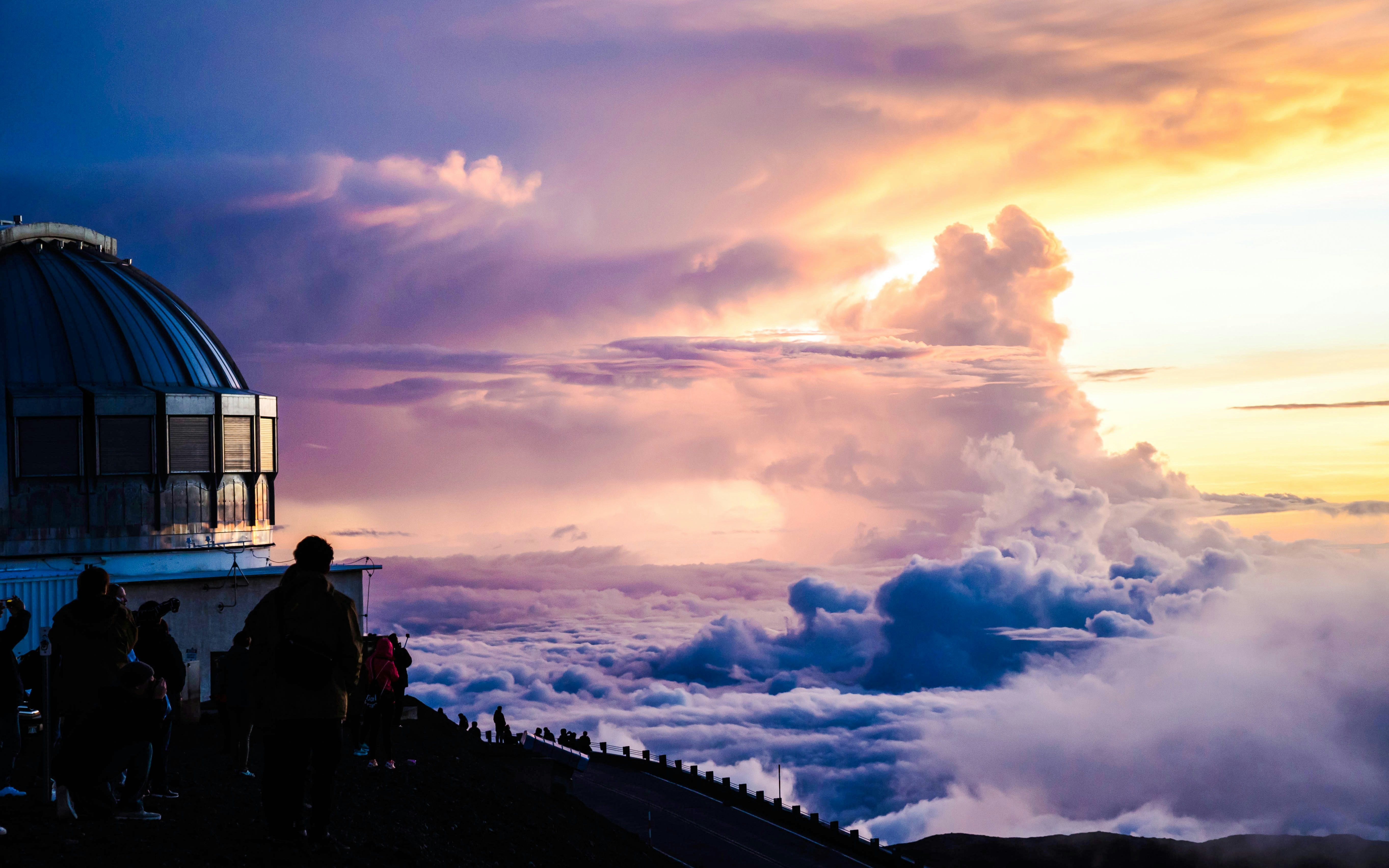 Mauna Kea observatories at sunset with clouds and visitors in Hawaii.