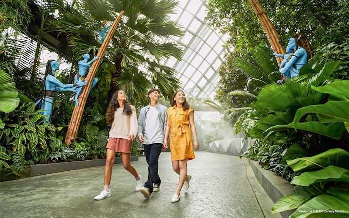 Visitors walking through lush greenery at Gardens by the Bay, Singapore, with Avatar-themed sculptures.