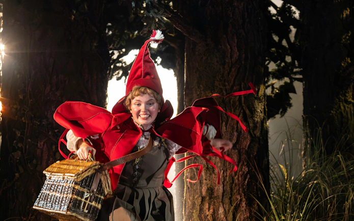Character in red costume running through a forest scene in "Into the Woods" performance.