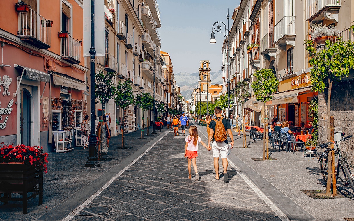 Pedestrians walking along Corso Italia in Sorrento, Italy, with shops and cafes lining the street.