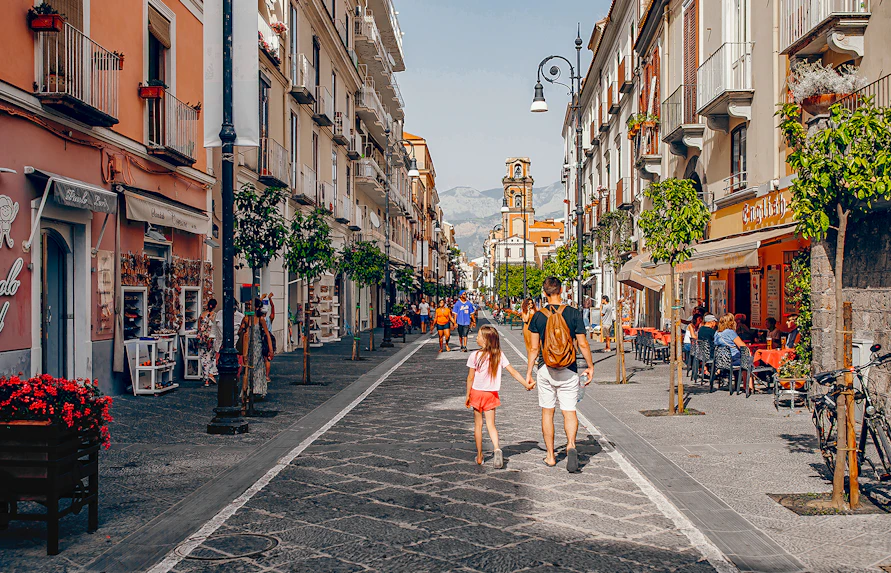 Pedestrians walking along Corso Italia in Sorrento, Italy, with shops and cafes lining the street.