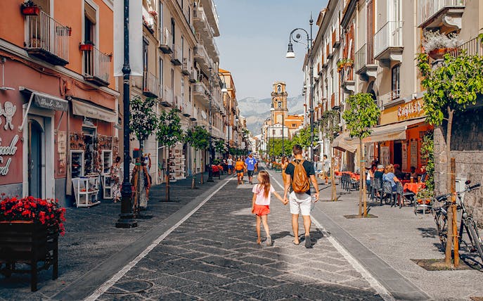 Pedestrians walking along Corso Italia in Sorrento, Italy, with shops and cafes lining the street.