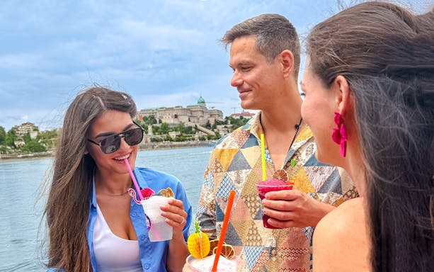 Guests enjoying slushies on Budapest Danube River sightseeing cruise with Buda Castle in view.