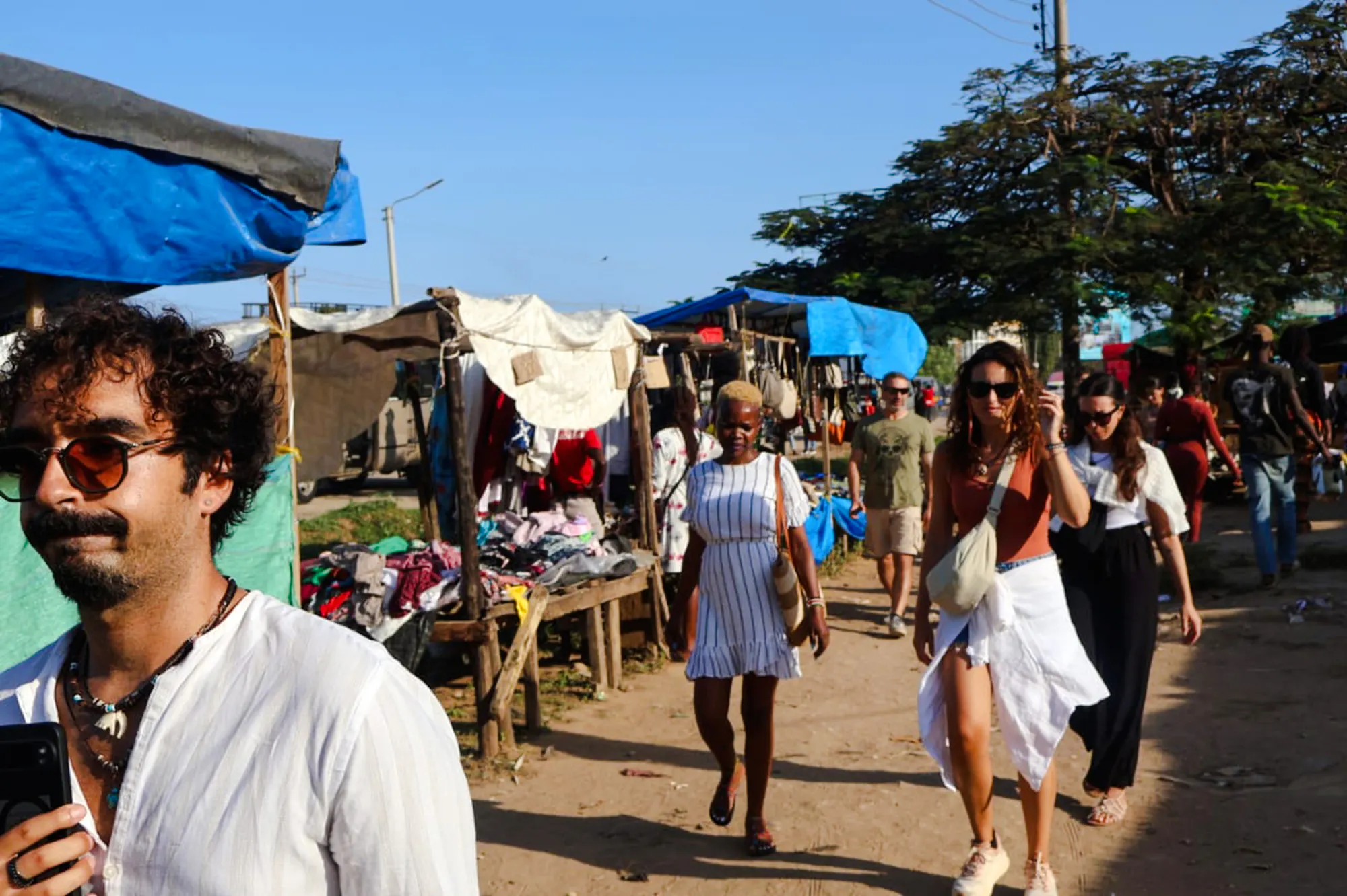 Local market scene in Diani Beach, Kenya, with people walking past stalls.