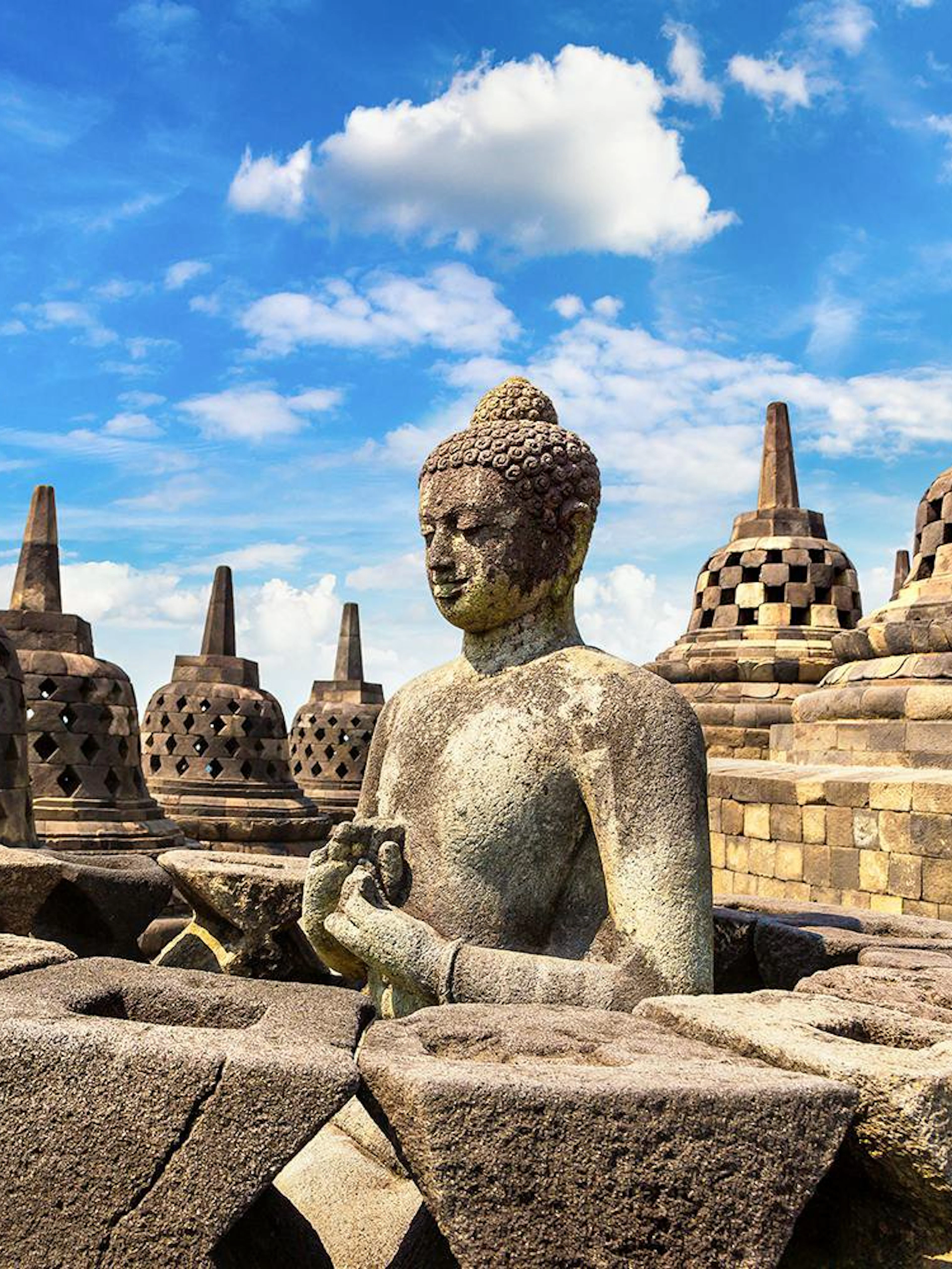 Buddha statue among stupas at Borobudur Temple, Java, under a clear blue sky.