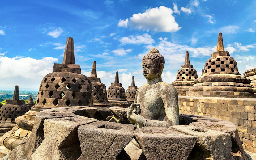Buddha statue among stupas at Borobudur Temple, Java, under a clear blue sky.
